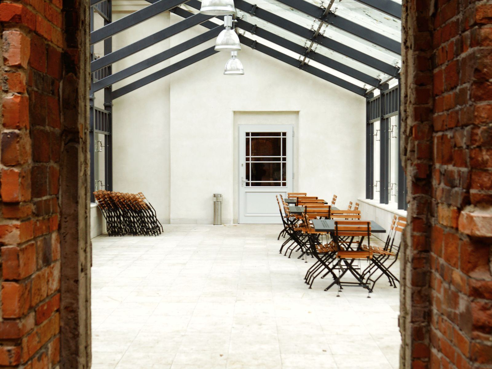 Indoor dining area with exposed brick walls and wooden furniture under a glass roof.