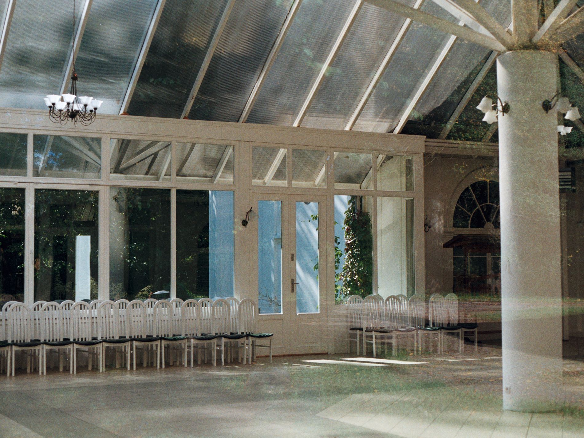 Large glass-roofed hall with rows of white chairs, ghosted double exposure.