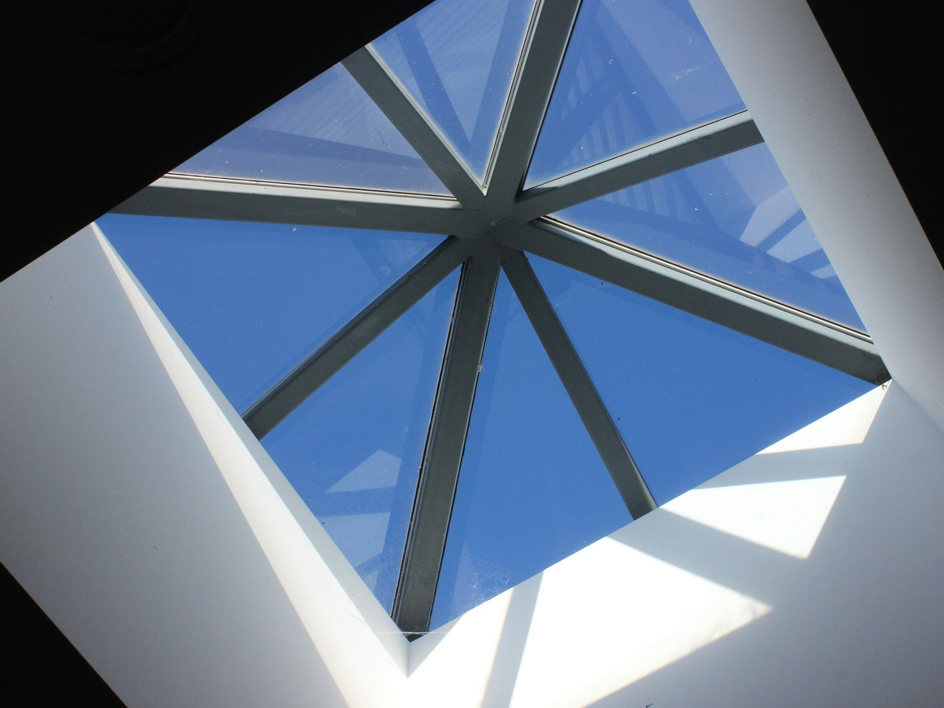 Pyramid-shaped skylight frame seen from below against a blue sky.