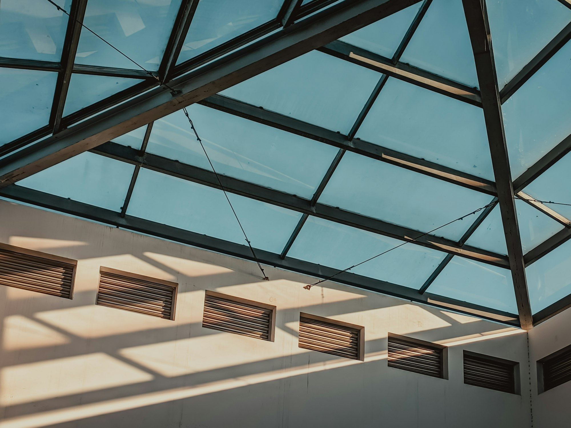 Interior view of a glass roof structure with sunlight streaming through.