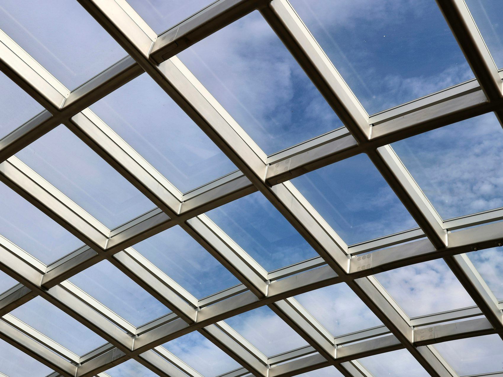 View of blue sky through a geometric glass roof structure.
